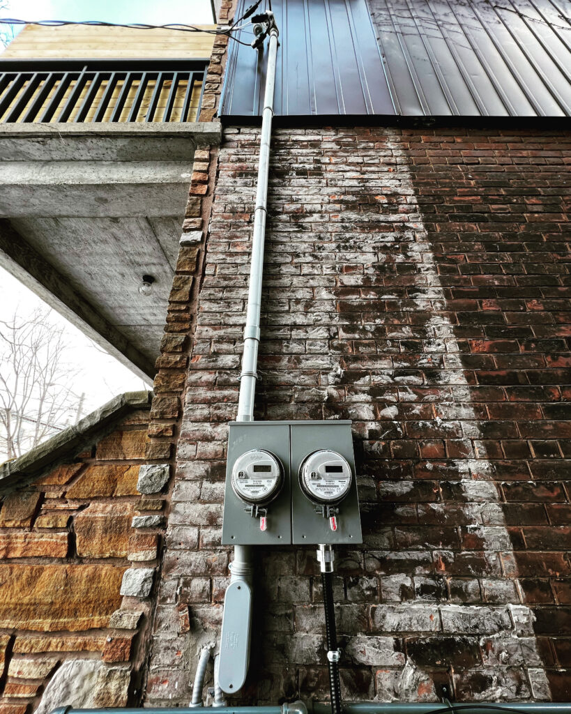 Two installed electrical meters and an overhead service mast on a brick exterior
