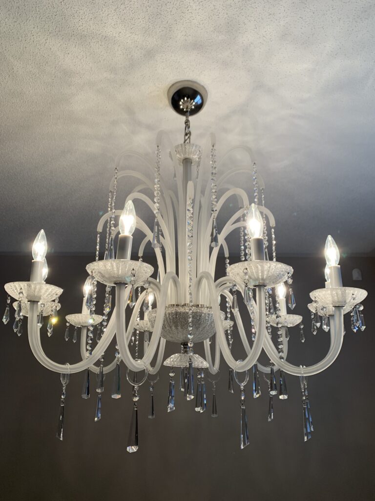 White chandelier with candle-style lamps and hanging crystal drops