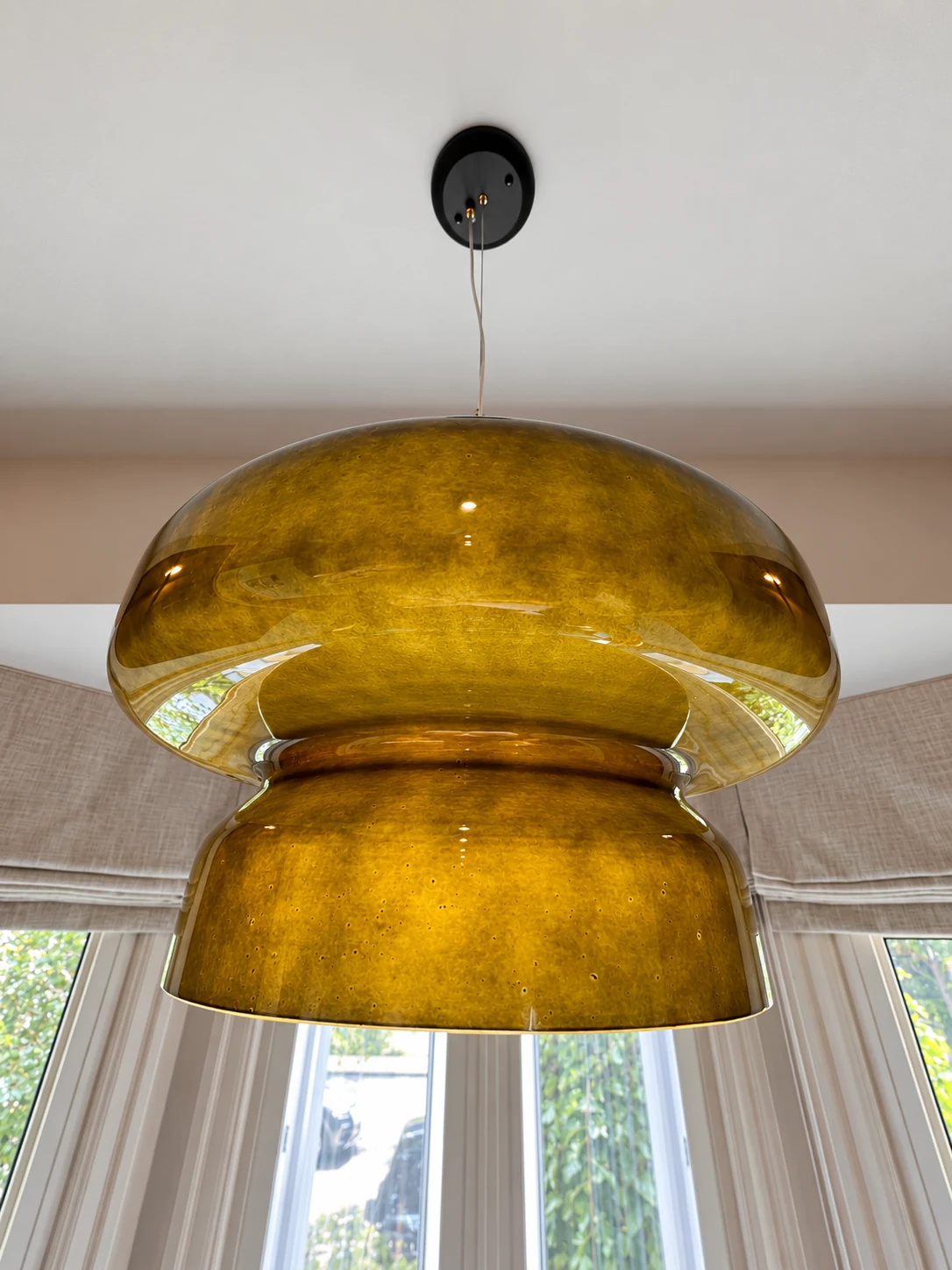 Close view of a sculptural amber glass pendant with a black ceiling canopy