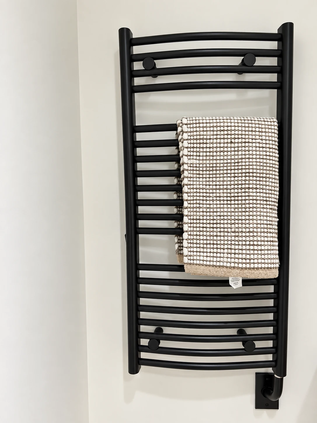 Wall-mounted black electric towel warmer with curved rails and a patterned towel