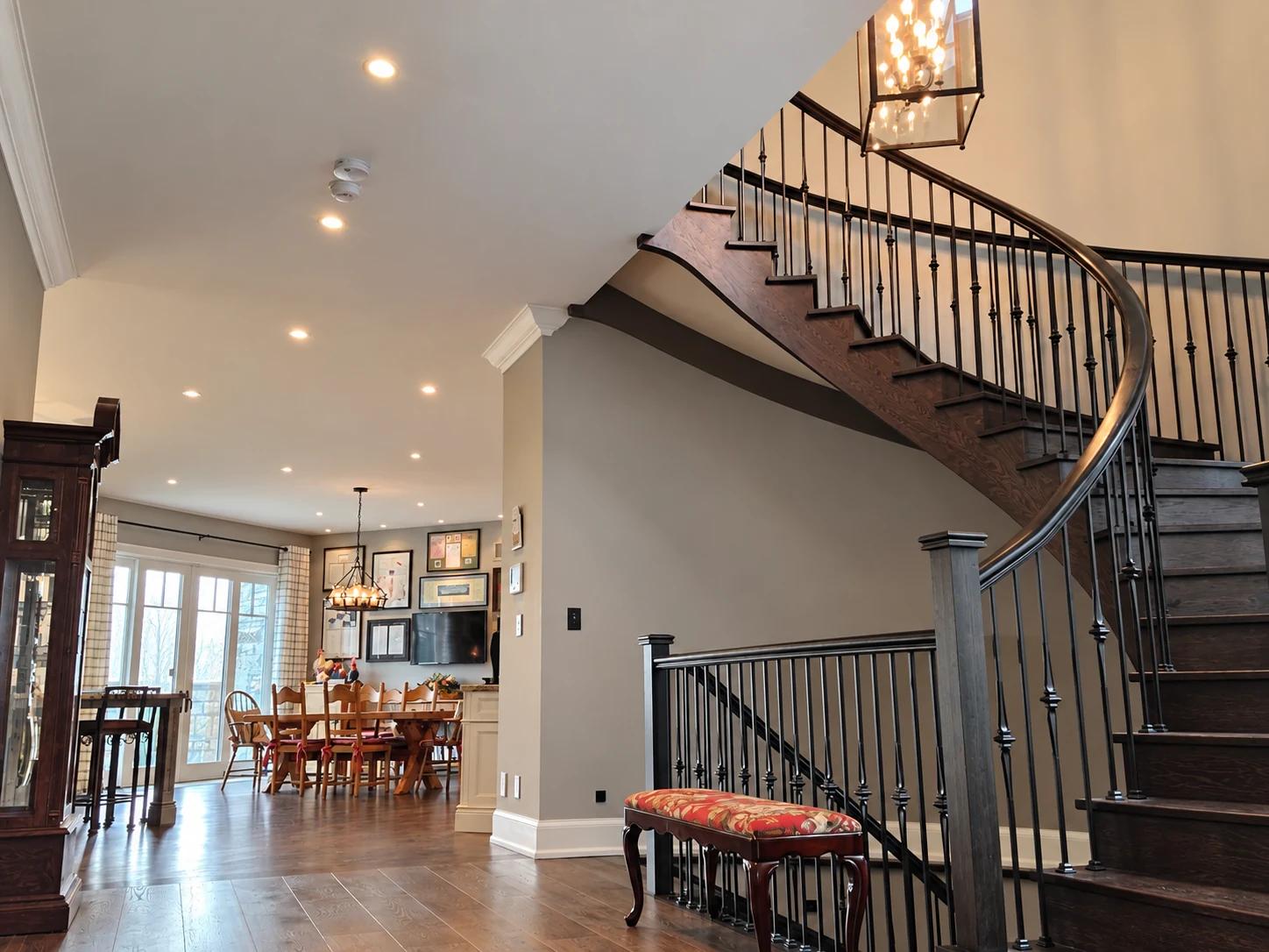 Curved wood staircase with lantern chandelier and recessed lighting extending into the dining area