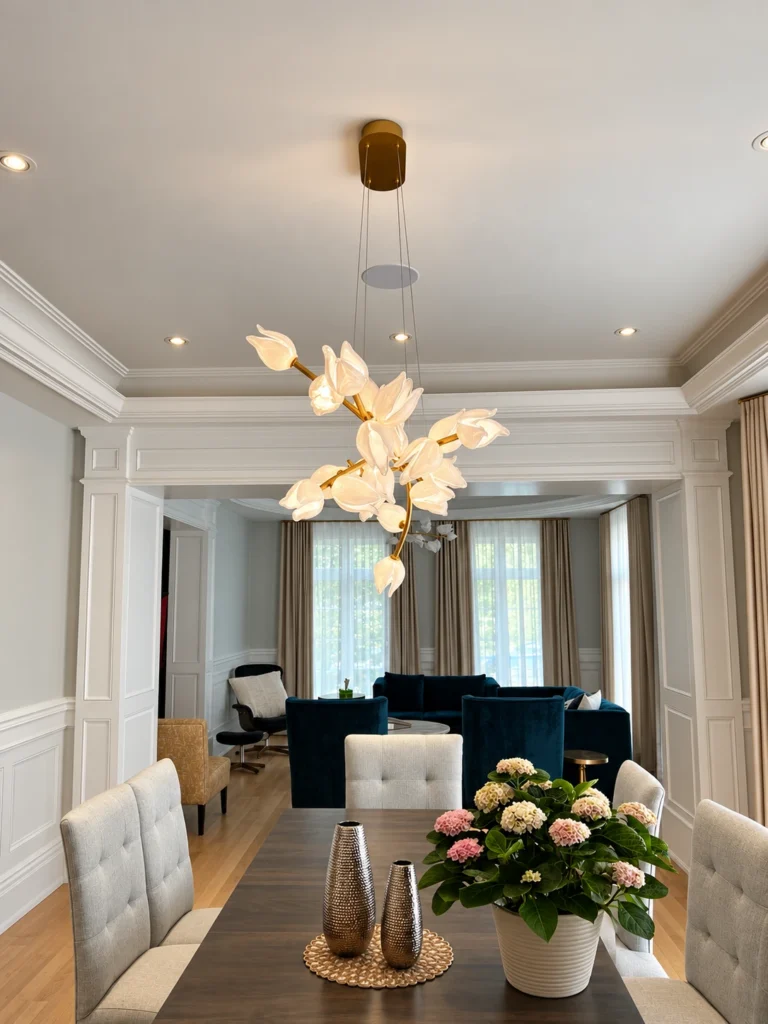 Side view of a sculptural floral glass dining chandelier beneath recessed lights and a ceiling speaker