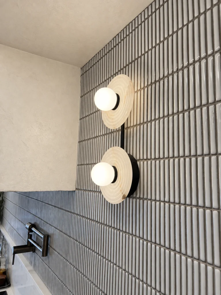 Double globe wall sconce with circular stone backplates mounted on grey vertical tile