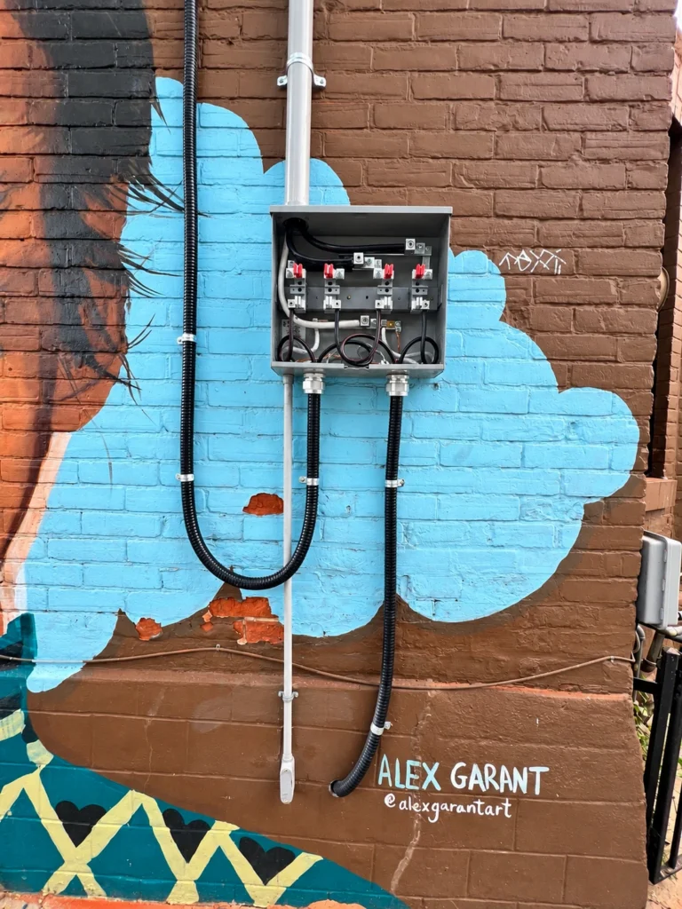 Open dual meter enclosure and conduits mounted on a painted brick wall