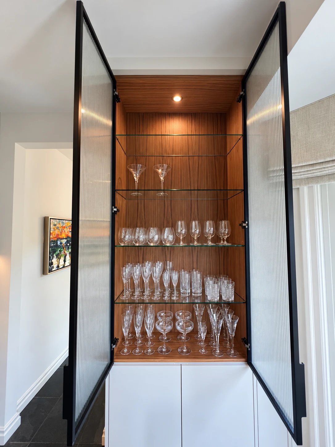 Illuminated wood display cabinet with glass shelves, glassware and open ribbed-glass doors