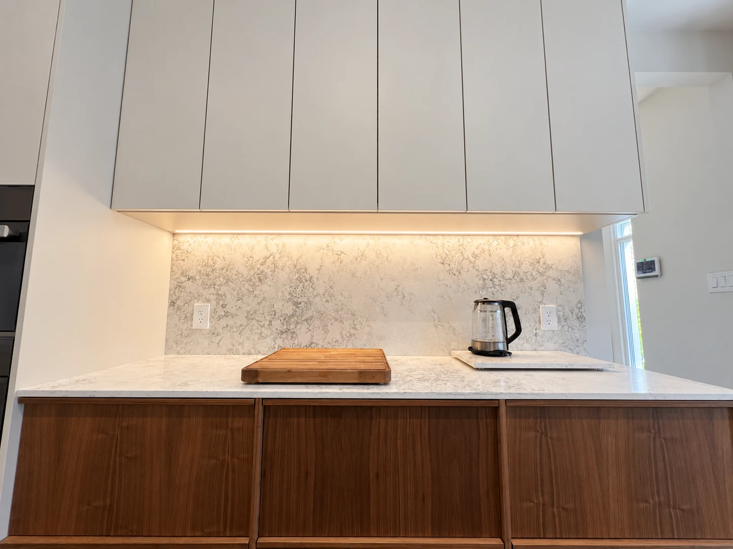 Under-cabinet LED lighting illuminating a marble kitchen backsplash and countertop
