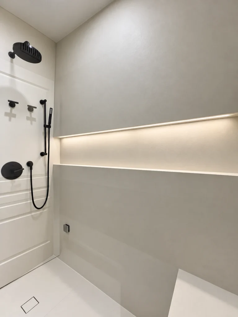 LED strip lighting illuminating a long shower niche beside matte black shower fixtures