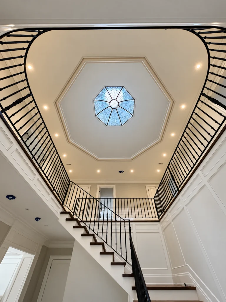 Recessed lighting around an octagonal skylight above a stairwell with black railings
