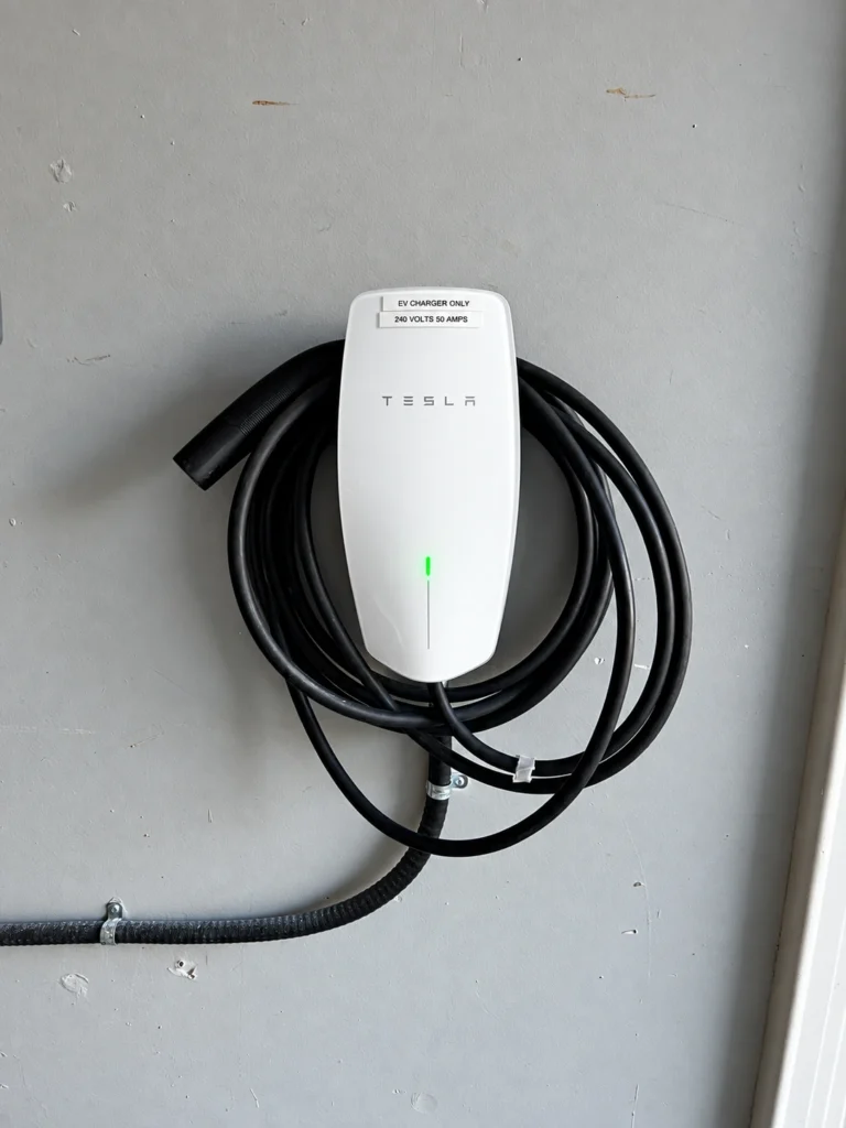 Wall-mounted Tesla EV charger with coiled charging cable and surface conduit